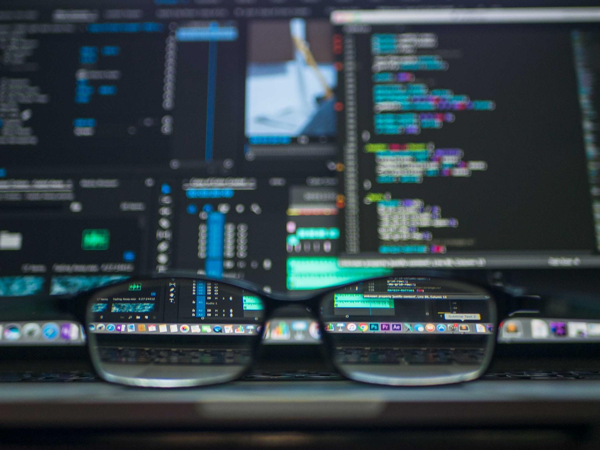 Pair of glasses placed infront of a monitor displaying code. The lens of the glasses have the image in focus.